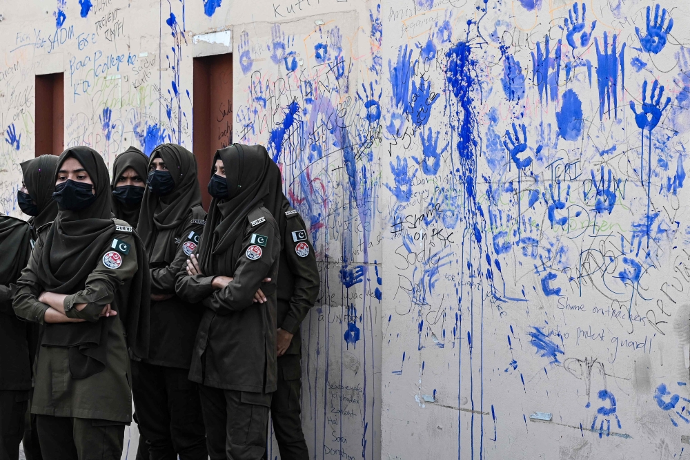 In this photograph taken on October 14, 2024, women police personnel stand guard beside a wall handprinted and scribbled by protesters during a demonstration to condemn the alleged rape of a woman student in Lahore. — AFP pic