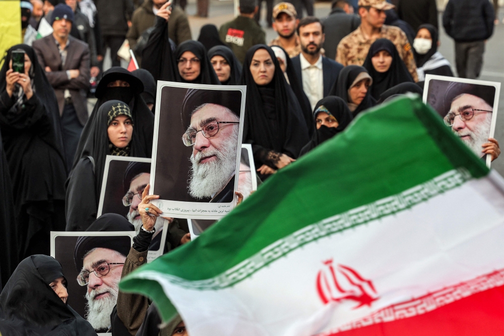 An Iranian flag flies before women demonstrators holding up pictures of Iran’s Supreme Leader Ayatollah Ali Khamenei during an anti-Israel rally in Tehran on October 24, 2024. — AFP pic