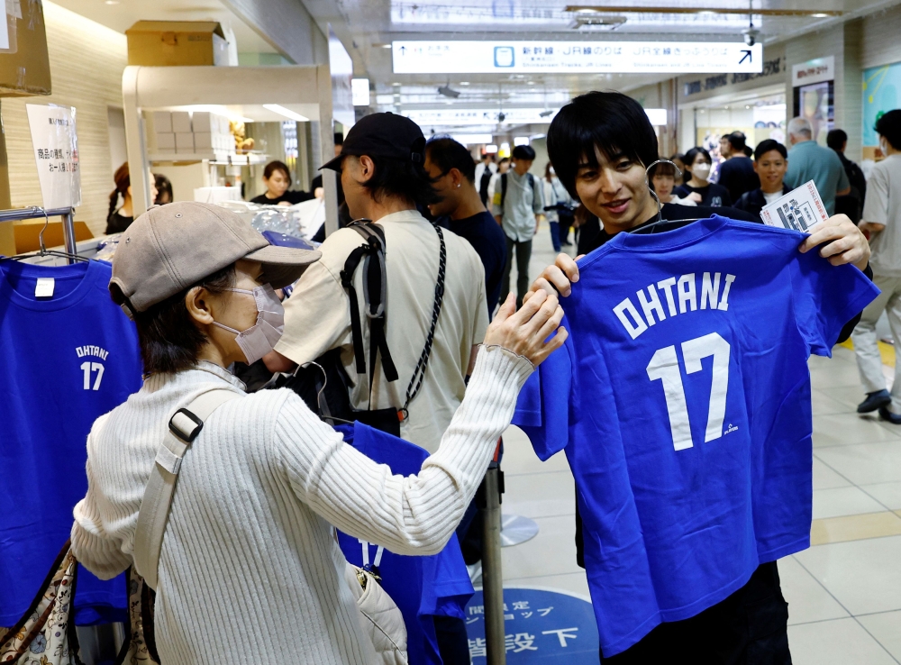 A clerk shows a T-shirt to a customer at a pop-up store for MLB star Shohei Ohtani ahead of the first World Series game between the Los Angeles Dodgers and the New York Yankees, in Tokyo October 25, 2024. — Reuters pic