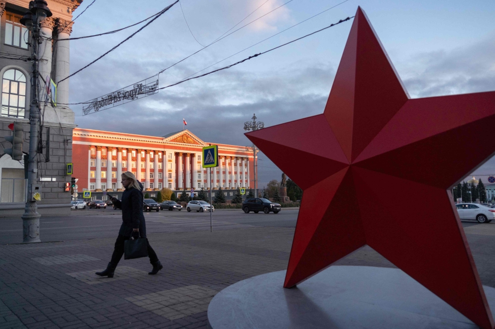 A woman walks past a red star installation, with the Kursk regional administration building seen in distance, in Kursk October 17, 2024. — AFP pic