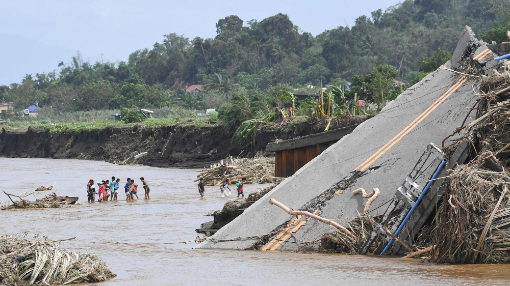 People cross a river next to a bridge that collapsed after the river overflew due to heavy rains brought about by Tropical Storm Trami in Laurel, Batangas province, south of Manila October 25, 2024. — AFP pic