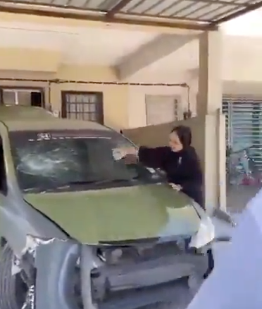 A screen capture from a viral video shows a woman smashing the windscreen of a vehicle being repossessed.