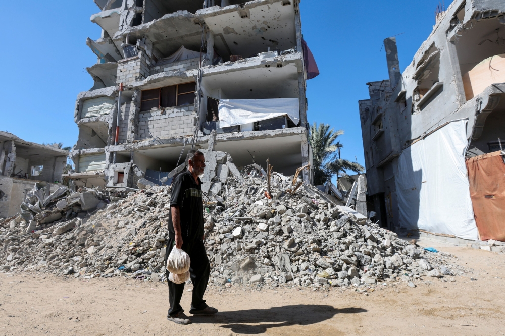 Displaced Palestinian man Khalil Al-Shannar walks past the rubble carrying bags of bread, amid the ongoing Israel-Hamas conflict, in Deir Al-Balah in the central Gaza Strip, October 24, 2024. — Reuters pic