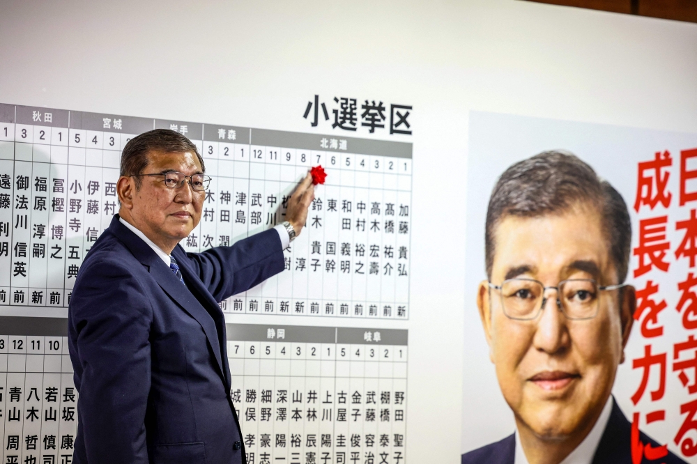 Japan’s Prime Minister Shigeru Ishiba places a rose pin above the name of a candidate at the Liberal Democratic Party (LDP) headquarters in Tokyo during the national election on October 27, 2024. — AFP pic