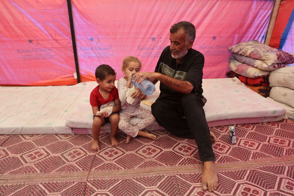 Displaced Palestinian man Khalil Al-Shannar gives water to a child in a tent where he shelters, amid the ongoing Israel-Hamas conflict, in Deir Al-Balah in the central Gaza Strip, October 24, 2024. — Reuters pic  