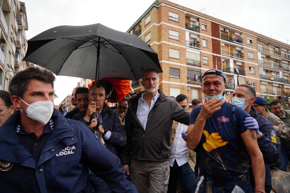 Security guards shielding King Felipe VI of Spain with an umbrella as angry residents heckle him and throw mud and objects during his visit to Paiporta. — AFP pic
