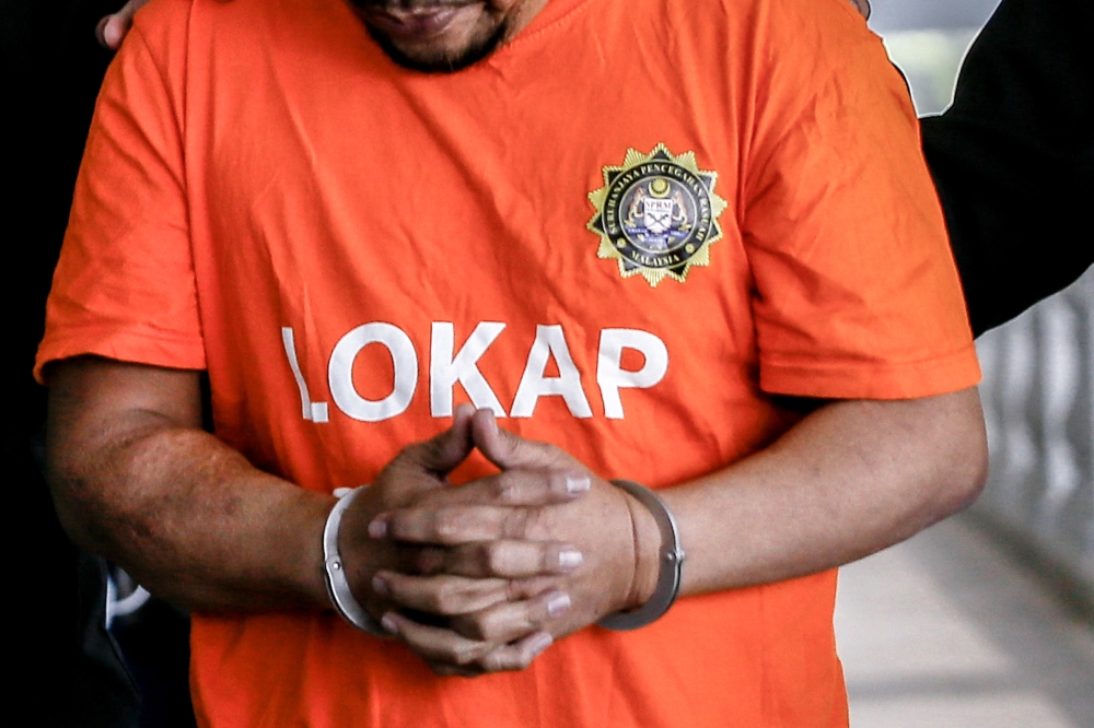 A man wearing the MACC’s signature orange detention garb is seen under escort at the Kuala Lumpur Court Complex on March 14, 2023. — File picture by Hari Anggara