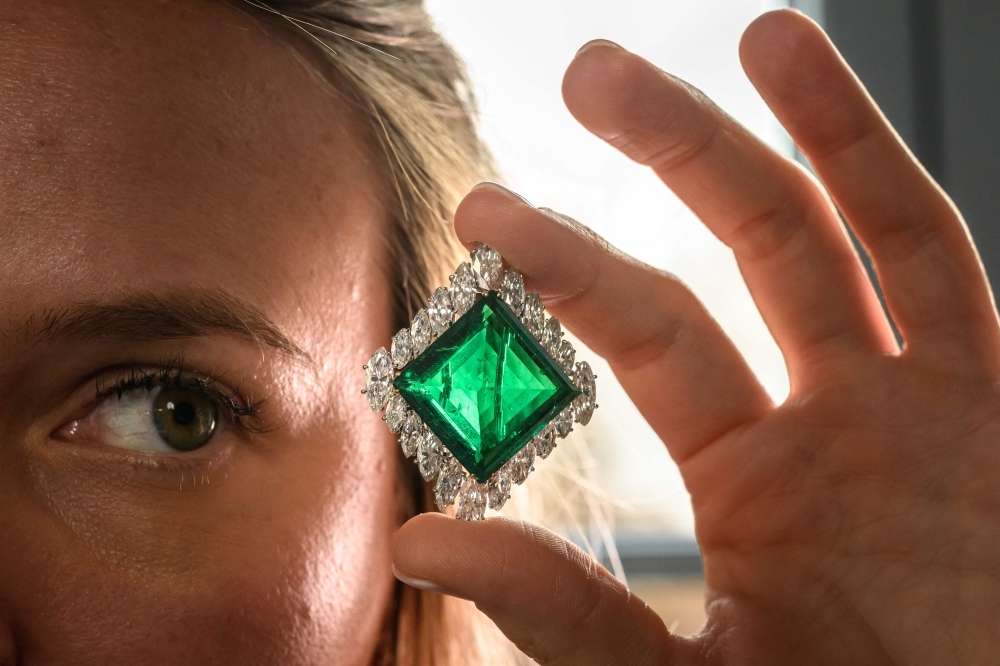 A Christie's employee poses with The Aga Khan Emerald, a cartier emerald and diamond brooch made with a square-shaped emerald of 37.00 carats, marquise-shaped diamonds, platinum and 18k yellow gold during a press preview in Geneva. — AFP pic
