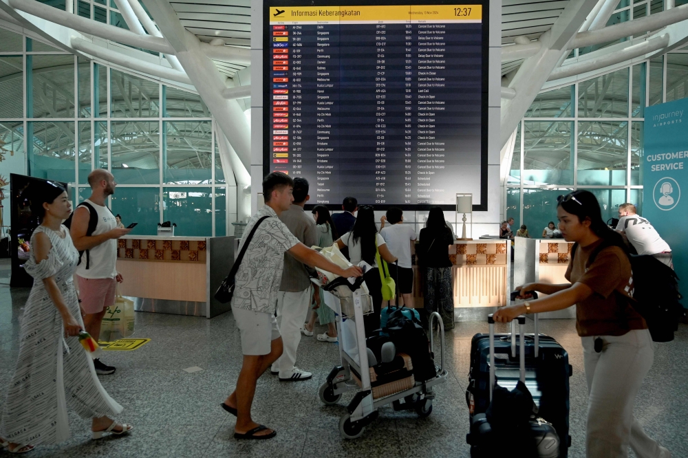 Passengers look at an electronic board displaying cancelled flights after Mount Lewotobi Laki-Laki volcano catapulted an ash tower miles into the sky, at the Ngurah Rai International Airport in Denpasar.— AFP pic
