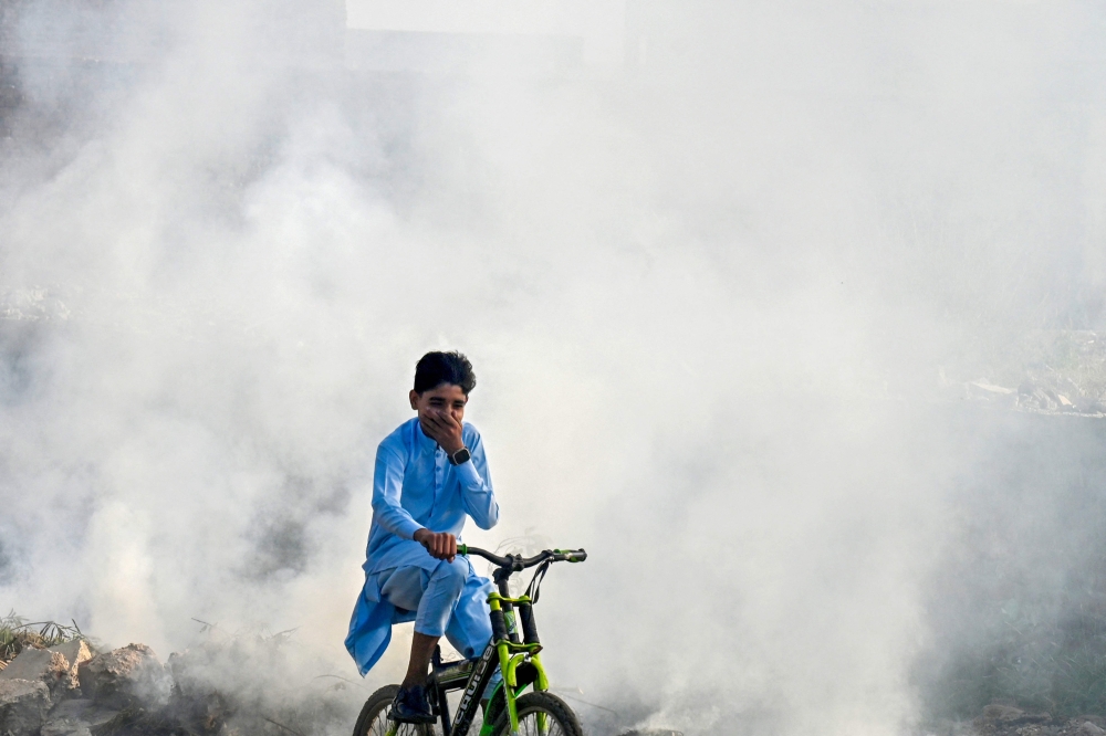 A boy rides past as smoke billows from a burning garbage dump, in Lahore on November 1, 2024. — AFP pic 