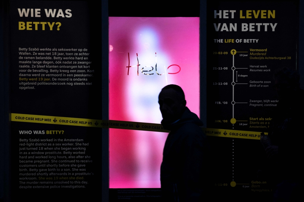 A pedestrian walks past a hologram screen representing a foggy window glass reading “help” and the silhouette of 19-year-old murdered sex worker Bernadette Szabo, known as Betty, implemented by Dutch police in hope to uncover new information around her murder, in Amsterdam, on November 15, 2024. — AFP pic