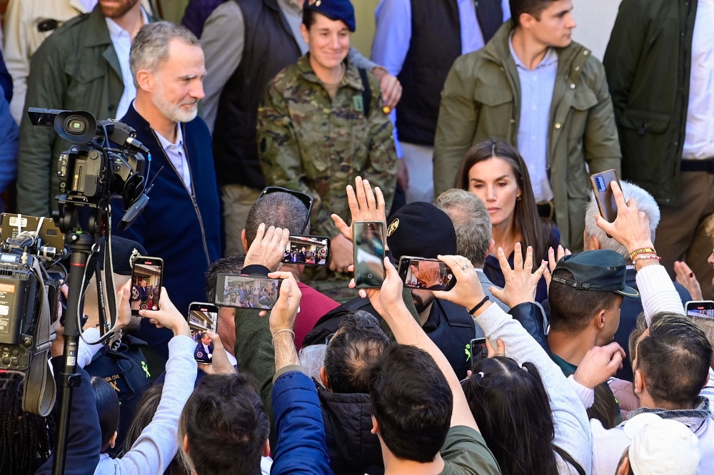 Residents hold up their phones to take photos of King Felipe VI (L) and Queen Letizia as they visit the flood damaged town of Chiva, in the region of Valencia. — AFP pic