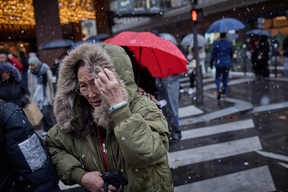 Pedestrians shelter from heavy snowfall during Storm Caetano in central Paris on November 21, 2024, as Paris is placed under the second highest weather warning by the French national weather service for snow. — AFP pic