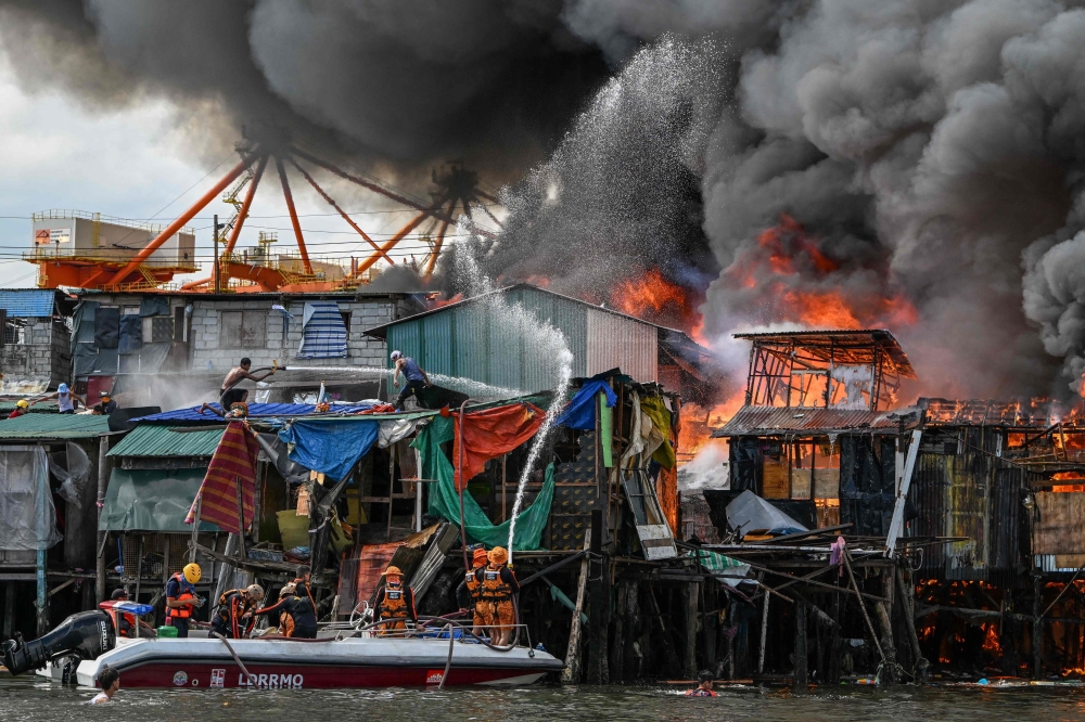 Raging orange flames and thick black smoke billowed into the sky Sunday as fire ripped through hundreds of houses in a closely built slum area of the Philippine capital Manila. — AFP pic