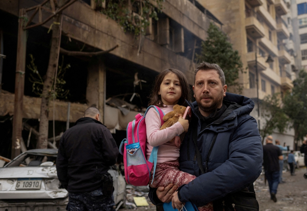 A man carries his daughter to her school as he walks past a damaged building in the aftermath of an Israeli strike, amid the ongoing hostilities between Hezbollah and Israeli forces, in Beirut’s Mar Elias street, Lebanon November 18, 2024. Lebanon has suspended in-person classes in the Beirut area for Monday, the education ministry announced on Sunday, citing safety concerns after a series of Israeli air strikes this week. –– Reuters pic 