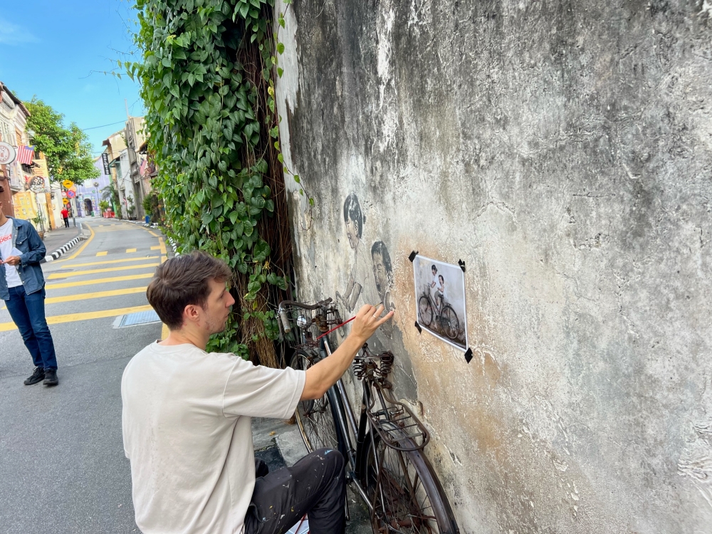 Ernest Zacharevic restoring the 'Children on Bicycle' mural in Armenian Street, George Town. — Picture by Opalyn Mok
