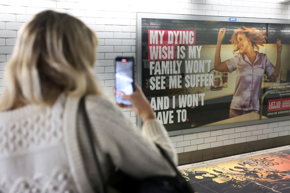 A tube passenger takes a photo of an assisted-dying rights billboard ahead of the parliamentary debate on Friday, in London, Britain November 26, 2024. — Reuters pic