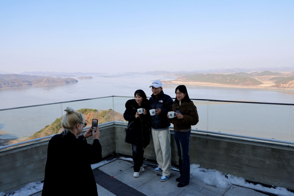 Customers holding a cup of coffee pose to take a picture with North Korea's propaganda village Kaepoong in the background, at the top of the Aegibong Peak Observatory, south of the demilitarized zone (DMZ), separating the two Koreas, in Gimpo, South Korea November 29, 2024. — Reuters pic  