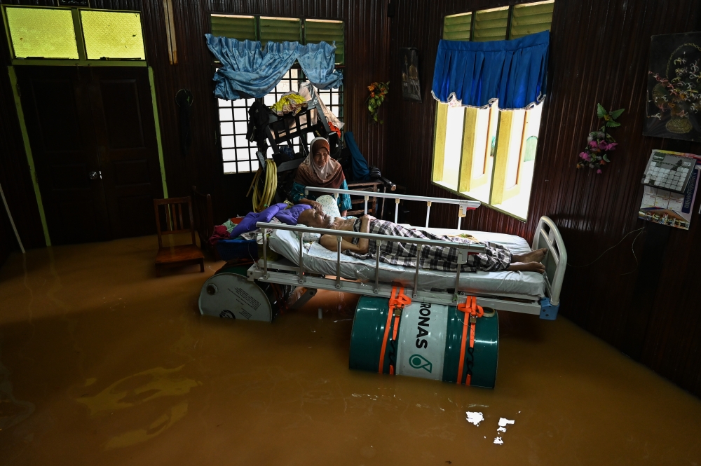 Zainab@Halimah Ismail, 77, cares for her ailing husband, Che Noh Che Hassan, 79, who lies on a bed floating with the help of metal drums in Kampung Chupu, Kuala Berang November 29, 2024. — Bernama pic