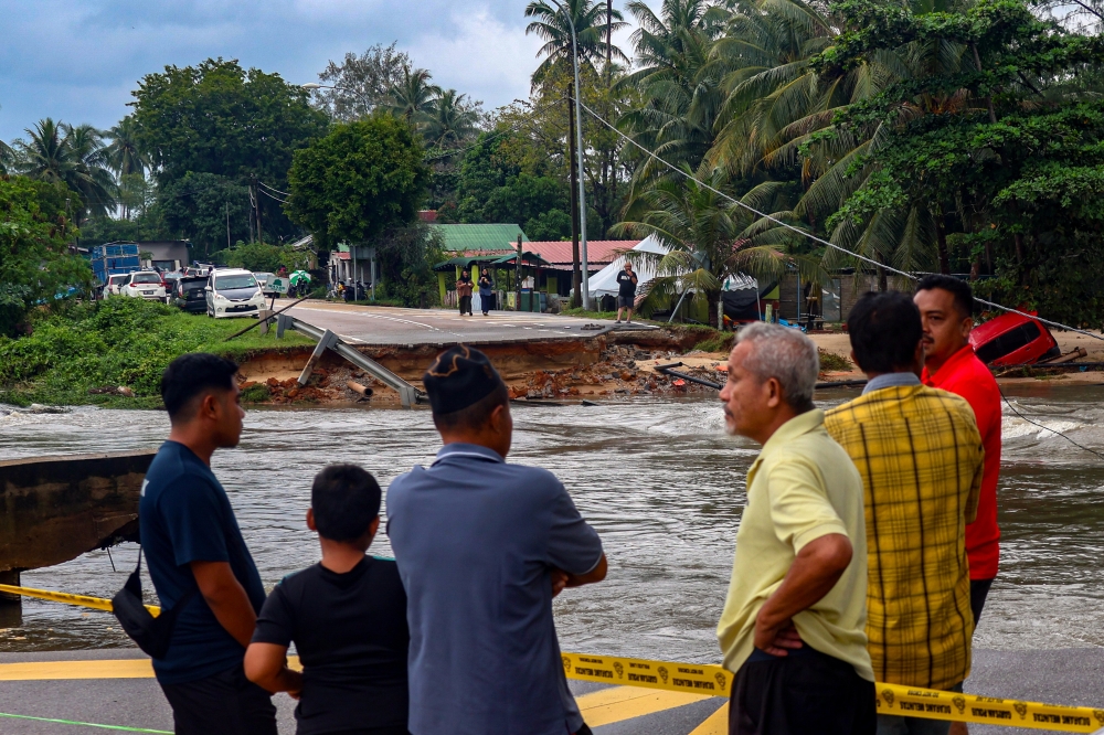 People stand near a washed out section of Jalan Kampung Tujuh near Taman Sri Bayu in Tumpat, Kelantan, on Dec 1, 2024. — Bernama pic