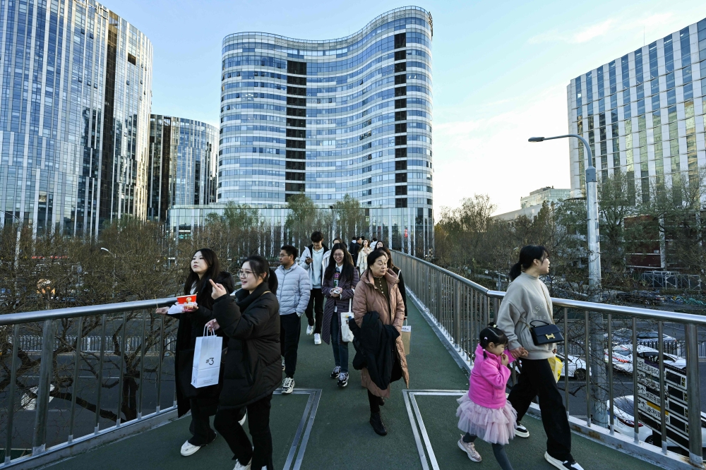 People walk along an overpass at the Sanlitun business area in Beijing on November 30, 2024. China’s housing market is in recovery mode after the government eased up rules limiting purchases. — AFP pic