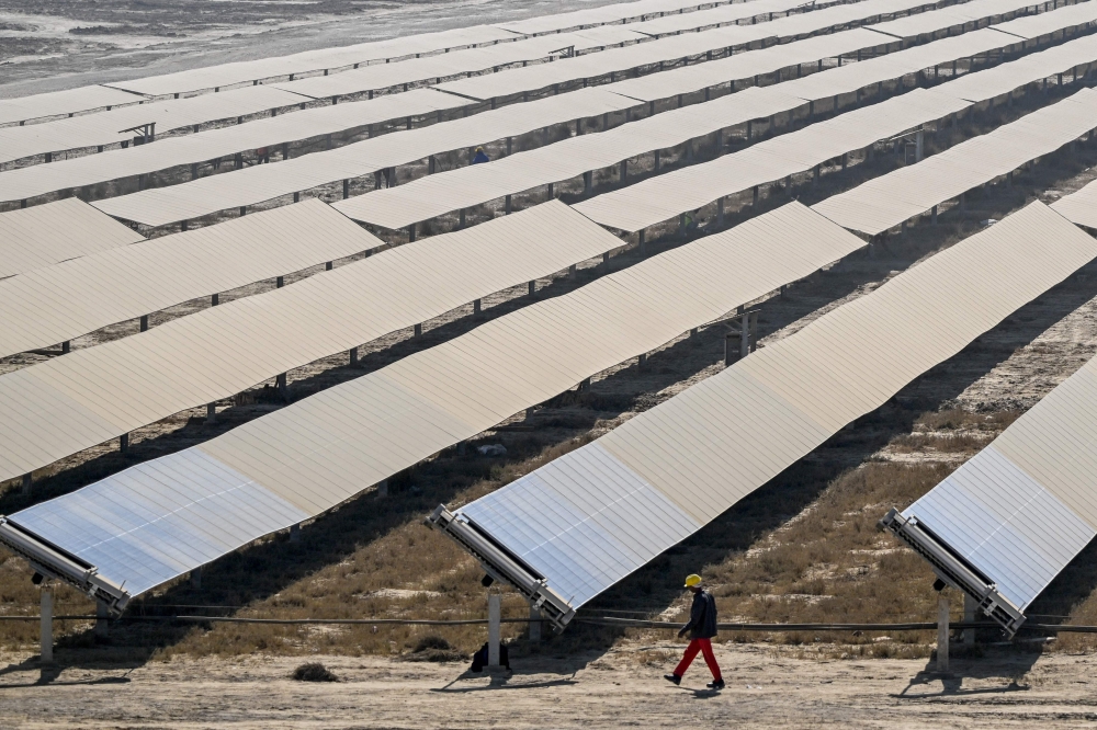 This photograph taken on January 12, 2024, shows a worker walking past rows of solar panels at the Adani Group owned Khavda Renewable Energy Park in Khavda. The Khavda plant in Gujarat state consists of some 60 million solar panels and 770 wind turbines spread over 538 square kilometres — almost the size of the sprawling megacity Mumbai. — AFP pic