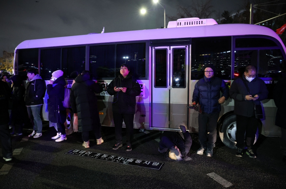 A woman lies on a road to block a vehicle transporting an army unit, after South Korean President Yoon Suk Yeol declared martial law, in Seoul, South Korea, December 4, 2024. — Reuters pic