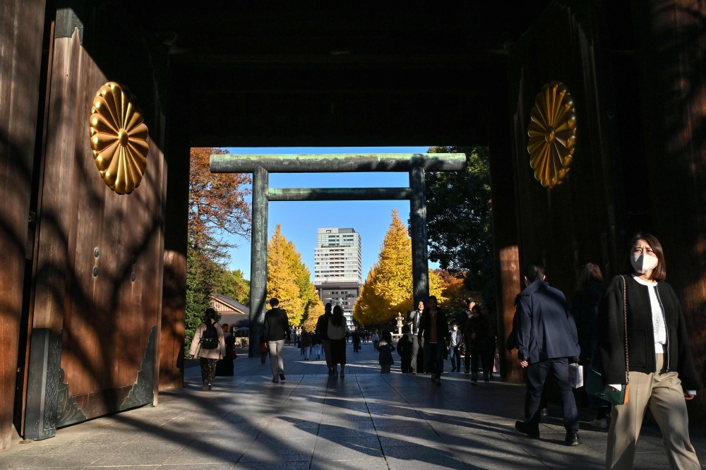 People walk through the entrance gates to Yasukuni Shrine as the leaves (behind) display a brilliant yellow colour for the autumn season in central Tokyo on December 1, 2024. Tokyo’s governor wants to introduce a four-day work week for government staffers in the capital as part of a nationwide push to encourage parenthood. — AFP pic 