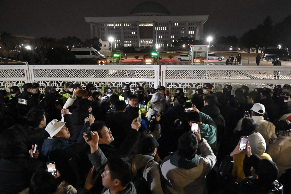 People gather in front of the main gate of the National Assembly in Seoul, South Korea on December 4, 2024, after President Yoon Suk Yeol declared emergency martial law. South Korean President Yoon Suk Yeol was still clinging to power today, with his party announcing they will oppose an opposition impeachment motion put forward after his stunning but brief imposition of martial law. — AFP pic