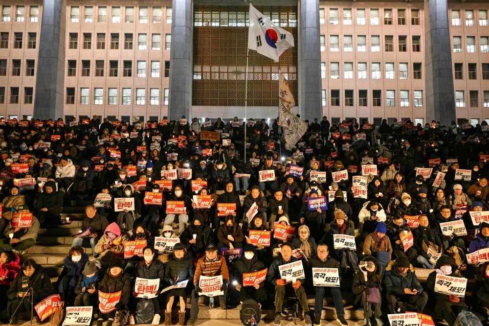 People call for the resignation of South Korea President Yoon Suk Yeol as they take part in a protest on the steps leading to the National Assembly in Seoul on December 4, 2024, as a South Korea flag flutters in the wind. South Korean prosecutors have opened an investigation into President Yoon Suk Yeol, his interior minister, and the now-former defence minister over their roles in an attempt to impose martial law, Yonhap news agency reported today. — AFP pic