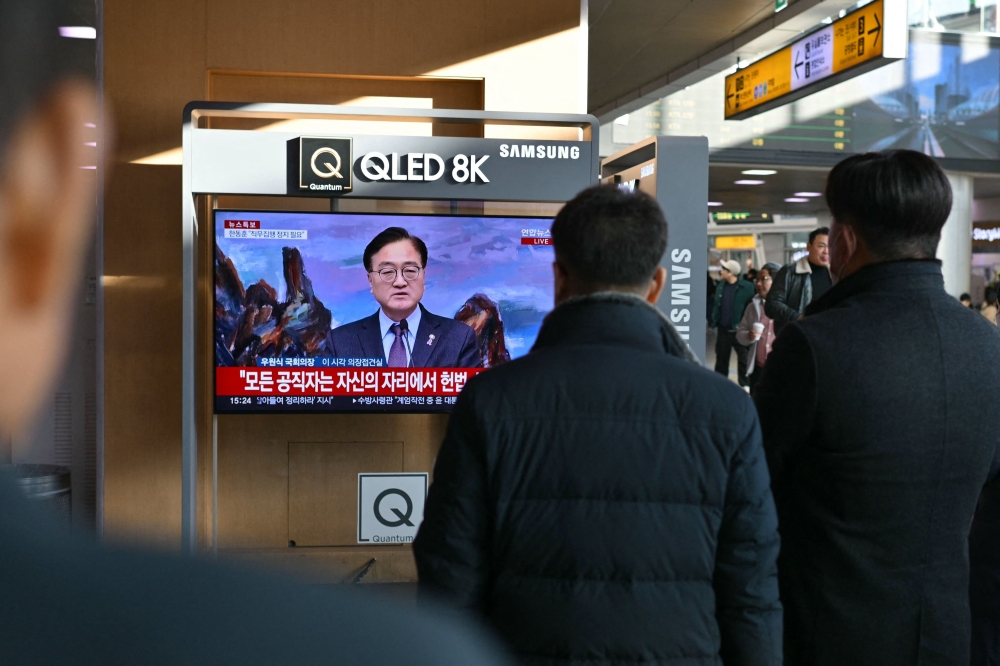 People watching a live television broadcast of National Assembly Speaker Woo Won-Shik speaking about South Korea President Yoon Suk Yeol at a train station in Seoul on December 6. — AFP pic