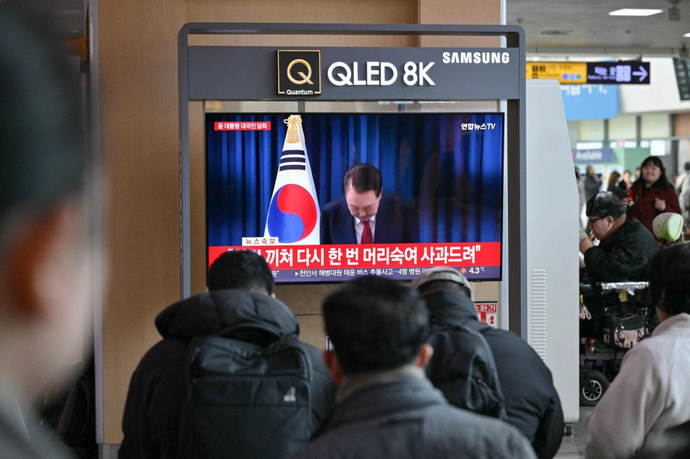 People watch a live television broadcast of South Korea's President Yoon Suk Yeol bowing after the end of his address, at a train station in Seoul on December 7, 2024. South Korean President Yoon Suk Yeol apologised yesterday for the confusion caused by his declaration of martial law and said he will let his party decide on his future position. — AFP pic