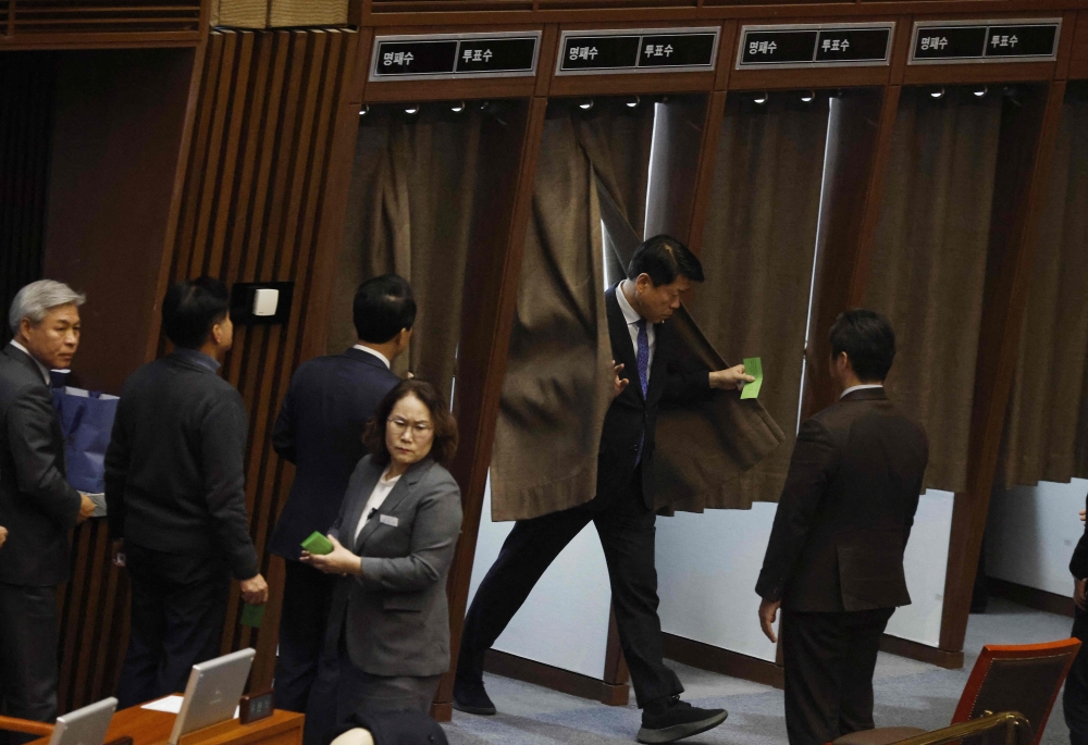 Lawmakers queue to cast their votes in polling booths on proposed legislation for appointing a special prosecutor to investigate allegations of stock price manipulation involving the president's wife during a plenary session for the impeachment vote of President Yoon Suk Yeol at the National Assembly in Seoul on December 7, 2024. — Jeon Heon-kyun/Pool/AFP pic