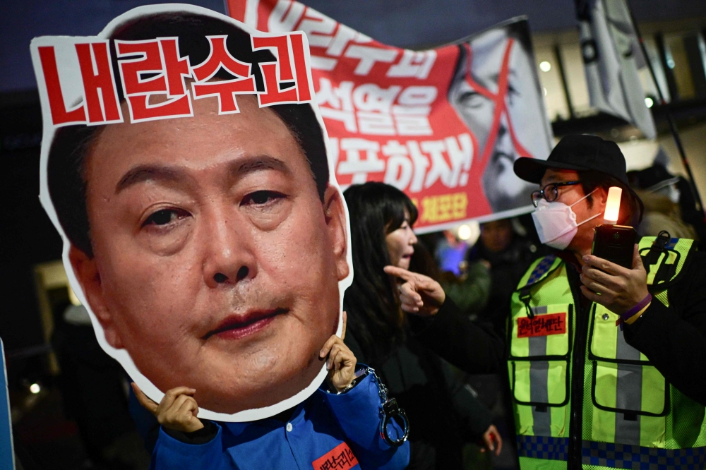 A protester holding a cardboard depicting the face of South Korea's President Yoon Suk Yeol takes part in a protest calling for his ouster outside the National Assembly in Seoul on December 8, 2024. — AFP pic