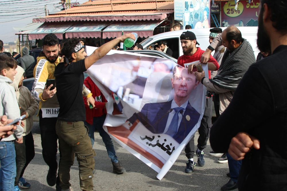 Syrian refugees hold a banner bearing a picture of President Bashar al-Assad with Arabic writing referring to him as a “pig” in the eastern Lebanese town of Majdel Anjar in the Bekaa Valley on December 8, 2024. — AFP pic