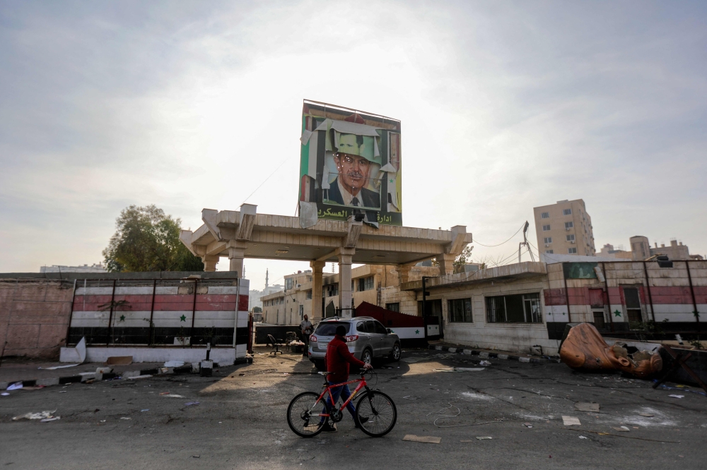 A man walks past a portrait of late Syrian president Hafez al-Assad in Damascus on December 9, 2024, after Islamist-led rebels seized the capital and forced President Bashar al-Assad to flee, ending five decades of Baath rule. — AFP pic