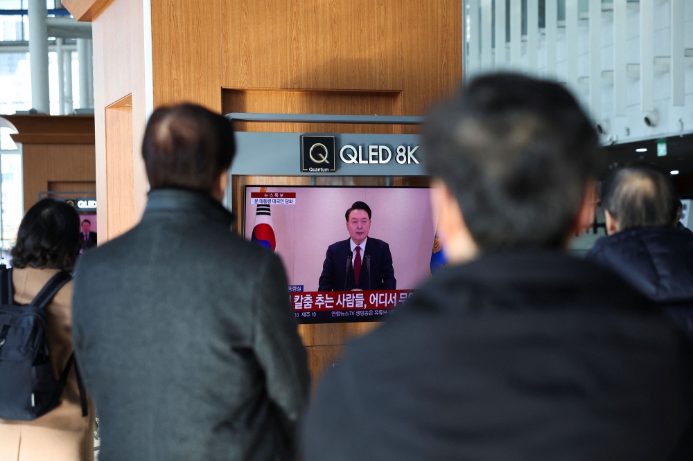 People watch a TV screen, broadcasting South Korean President Yoon Suk Yeol delivering an address to the nation, at a railway station in Seoul December 12, 2024. — Reuters pic  