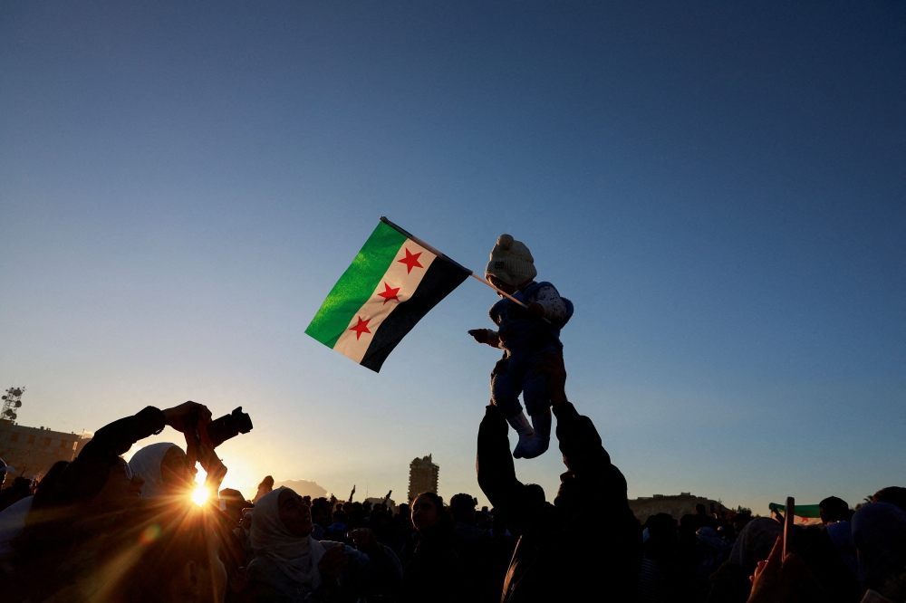 A child holding the flag adopted by the new Syrian rulers is held up, as people celebrate after fighters of the ruling Syrian body ousted Syria's Bashar al-Assad, in the Damascus old city, Syria, December 13, 2024. — Reuters pic