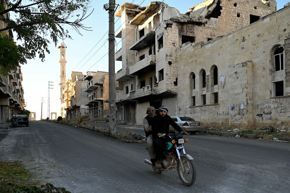 A Syrian man rides his motorcycle past destroyed buildings in Maaret al-Numan, in the northwestern Syrian Idlib province, on December 14, 2024. — AFP pic