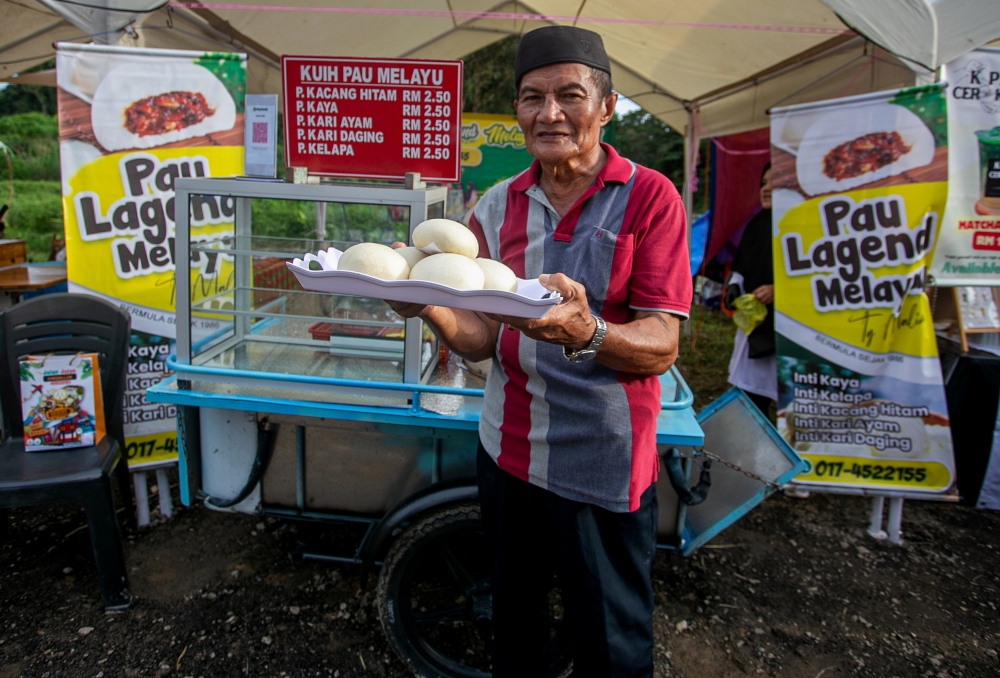 Surdi Maris, 72, showcases the Kuih Pau sold at his stall during the Pau Festival X Muallim Recreation 2024 event at the Bernam River waterfront in Tanjung Malim December 15, 2024. — Bernama pic