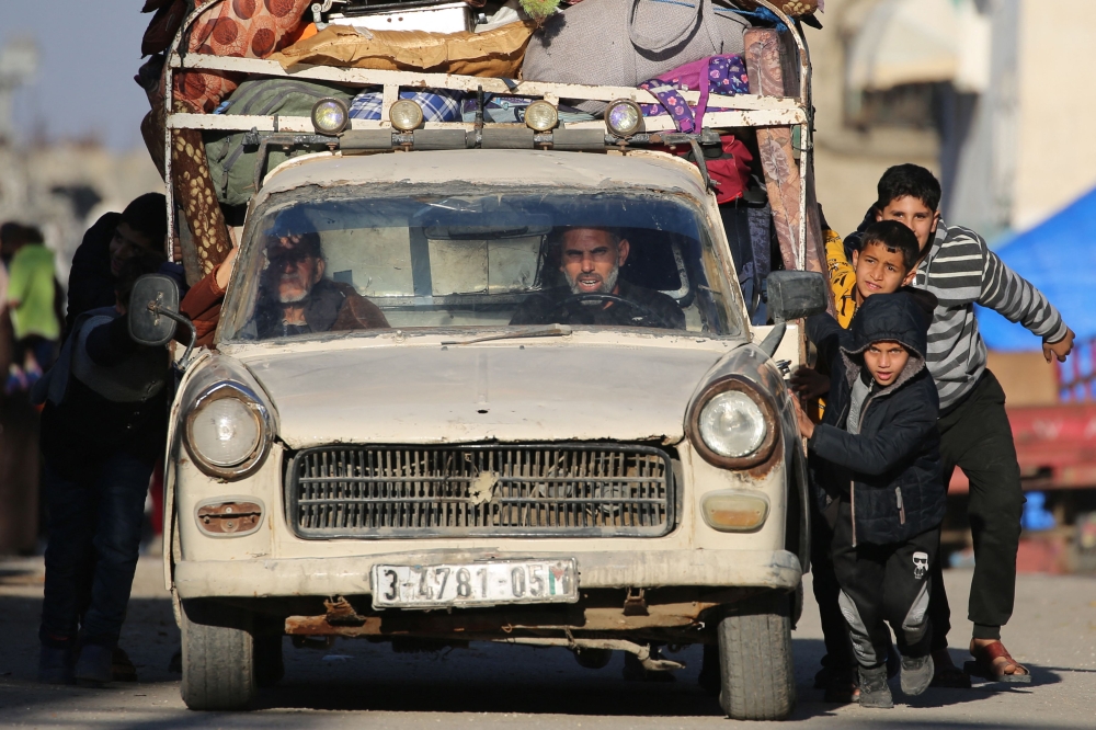 Palestinian children help push a car as people evacuate from their homes with their belongings, after receiving evacuation orders from the Israeli military. — AFP