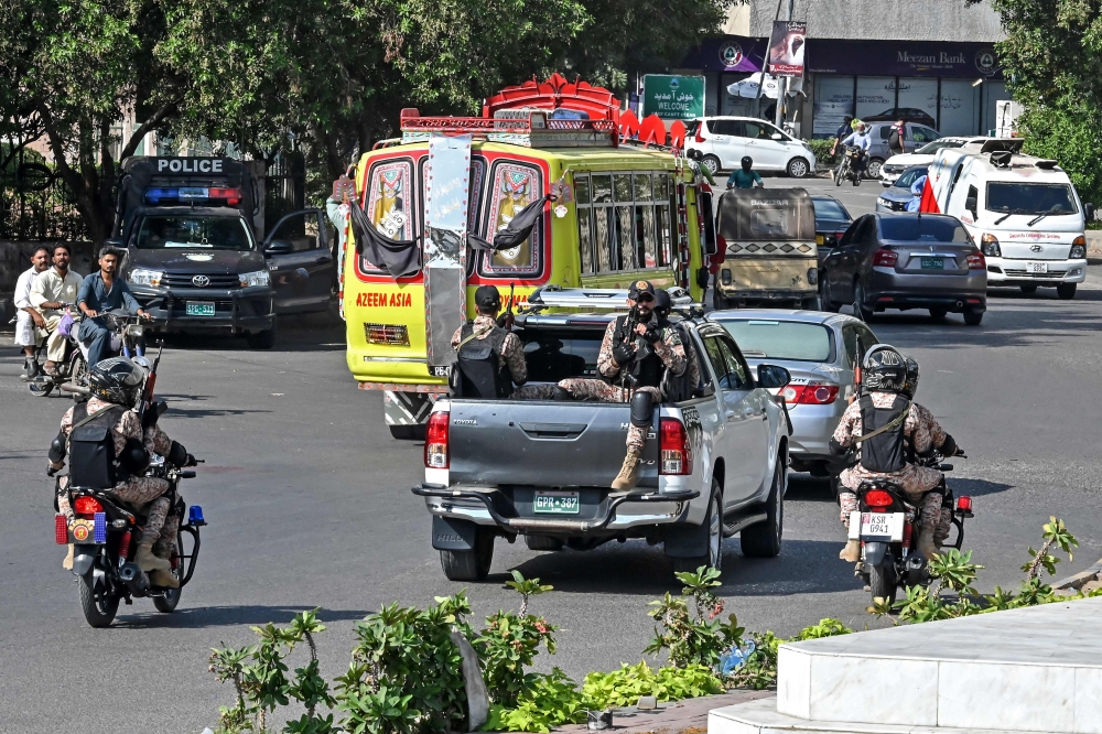 This photograph taken on November 12, 2024 shows paramilitary personnel riding on the back of a Toyota Hilux pick-up truck (centre) locally known as 'Dala', as they patrol along a street in Karachi. — AFP pic