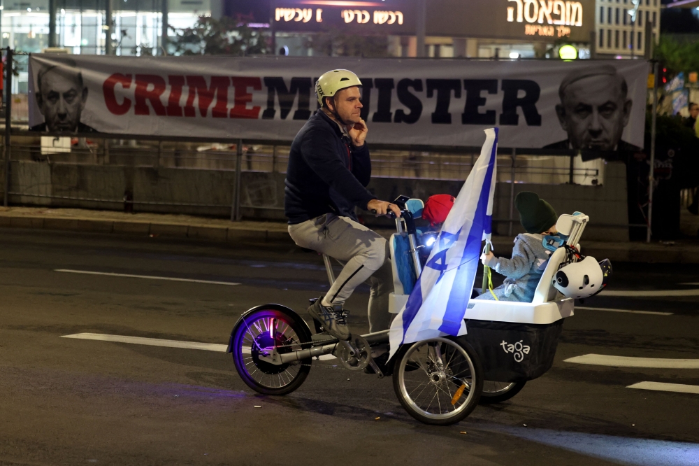 A demonstrator rides a tricycle past a banner in Tel Aviv bearing the image of Israeli Prime Minister Benjamin Netanyahu during a December 21, 2024 anti-government protest calling for action to secure the release of Israeli hostages held captive since the October 7 by Palestinian militants in the Gaza Strip. — AFP pic