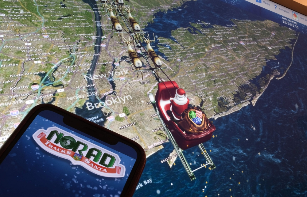 This illustration photo shows the NORAD logo on a cell phone screen while the tracker follows Santa flying over New York City on a computer monitor in Los Angeles on December 24, 2023. — AFP pic