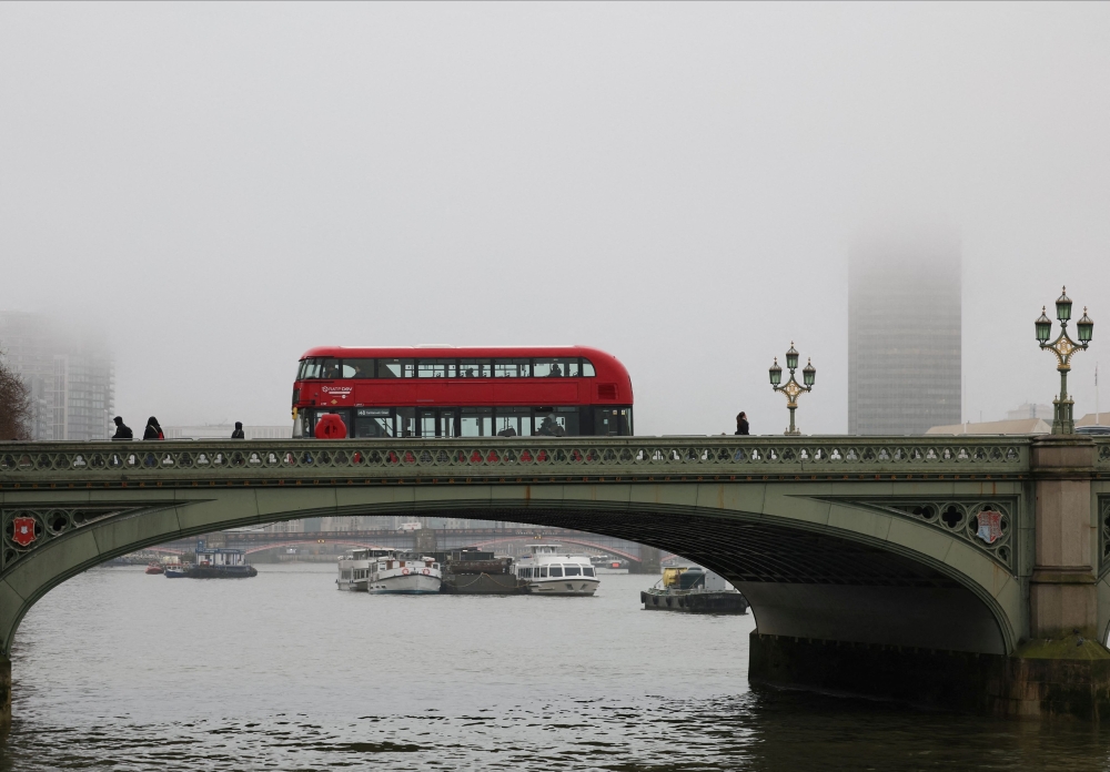 A red double-decker bus crosses Westminster Bridge amidst thick fog in London. — Reuters pic