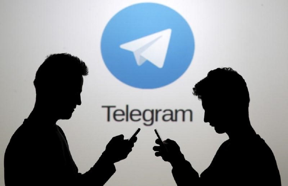 Men posing with their smartphones in front of a screen showing the Telegram logo. — Reuters pic