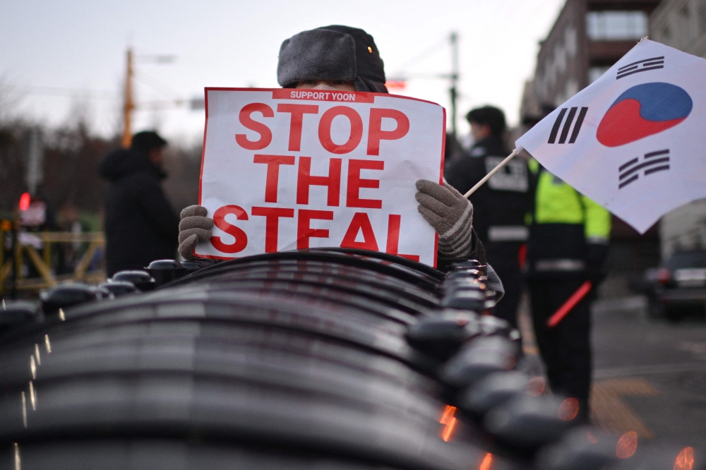 A supporter of impeached South Korean president Yoon Suk-yeol holds a South Korean flag and a sign reading ‘Stop the steal’ during a rally near his residence in Seoul January 9, 2025. — AFP pic