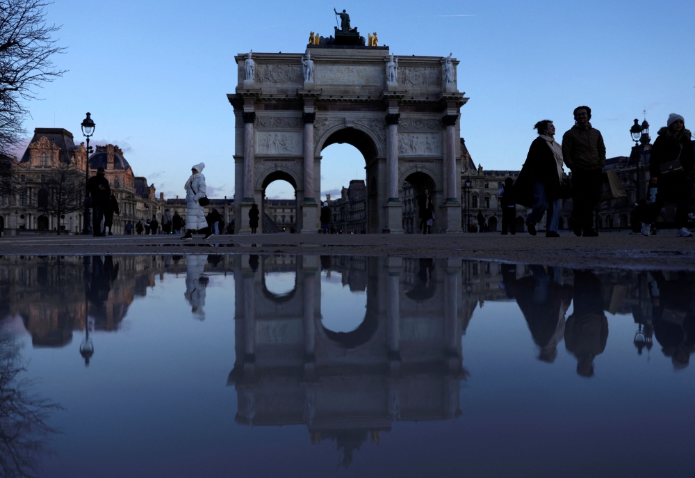 The Arc de Triomphe du Carrousel is reflected in a puddle as tourists walk near the Louvre museum on a winter day in Paris, France, January 9, 2025. — Reuters pic