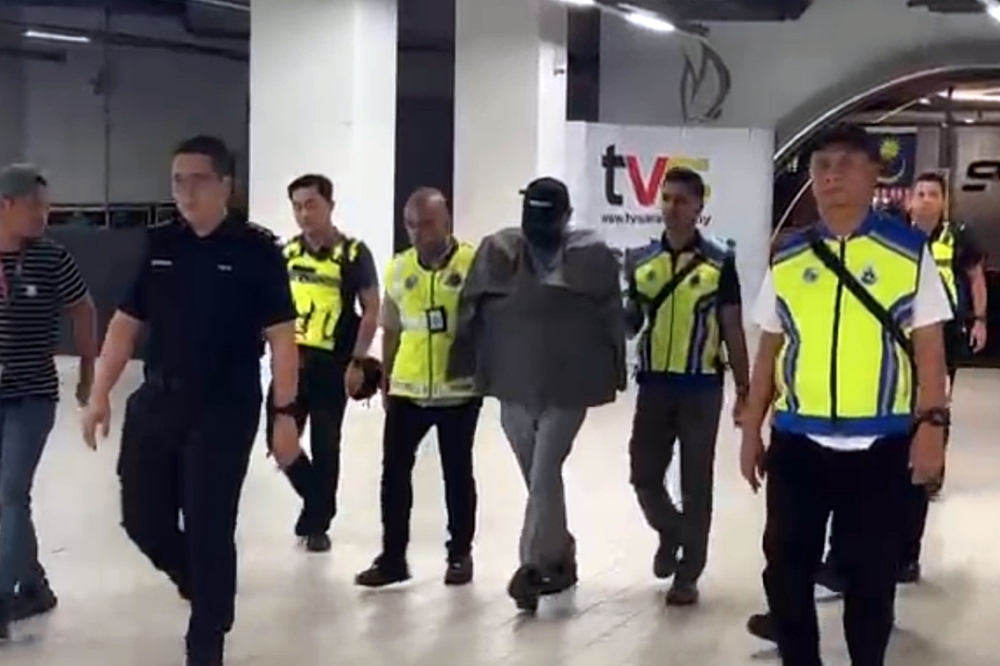 The senior executive being escorted by police at TVS headquarters in Kuching. – Screengrab by The Borneo Post