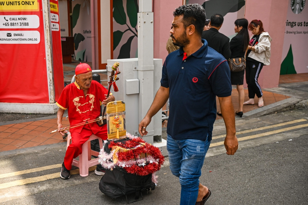 A man walks past a busker playing violin on the street in the Chinatown district of Singapore on January 7, 2025. — AFP pic
